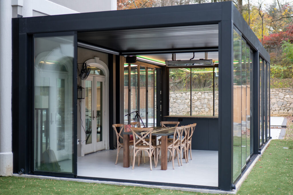 Modern black aluminum louvered pergola with sliding glass walls creating an enclosed outdoor dining space in Chantilly Virginia