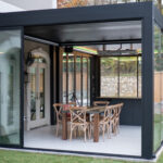 Modern black aluminum louvered pergola with sliding glass walls creating an enclosed outdoor dining space in Chantilly Virginia