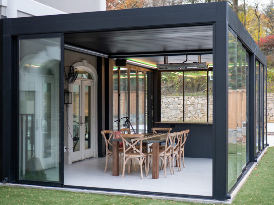 Modern black aluminum louvered pergola with sliding glass walls creating an enclosed outdoor dining space in Chantilly Virginia